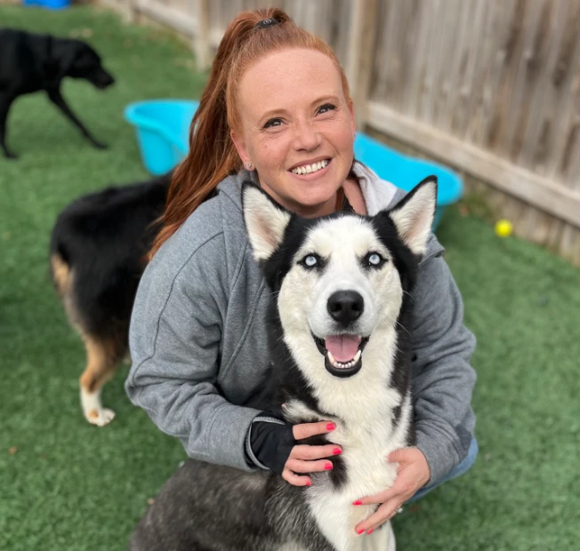 Sarah, Pawsh Park's Lead Trainer, smiling with a husky in the play yard